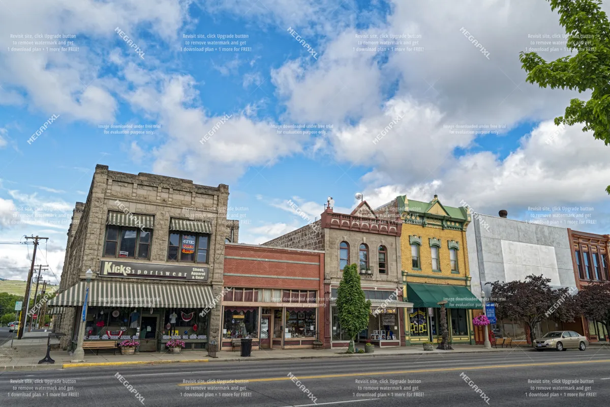 A vibrant stretch of historic downtown Baker City, featuring colorful building facades, inviting storefronts, tree-lined sidewalks, and people leisurely strolling and dining at outdoor cafes.
