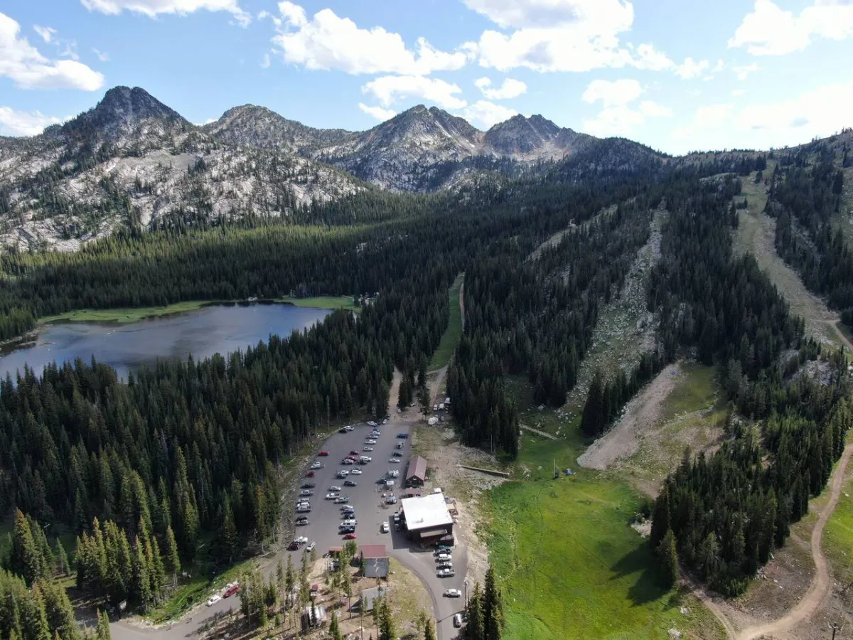 A scenic landscape shows a serene lake framed by majestic mountains, with a lodge and a small parking area nearby. The setting is inviting for hiking, picnicking, and nature exploration, capturing the expansive beauty of the area.