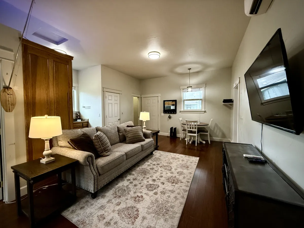 A comfortable, inviting living area featuring a plush sofa, soft lighting from a lamp, a TV, and a dining table set for meals or activities, all arranged in an intimate, single-level space.