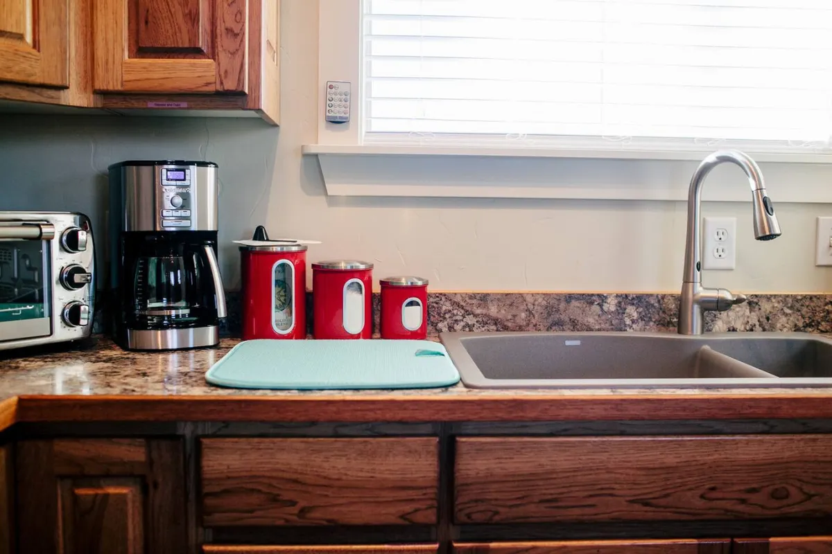 A countertop scene displaying a coffee maker, toaster oven, red canisters, and a sink, evoking a sense of morning rituals and casual meal prep. The area is cozy and functional, ideal for quick breakfasts or leisurely brunches.
