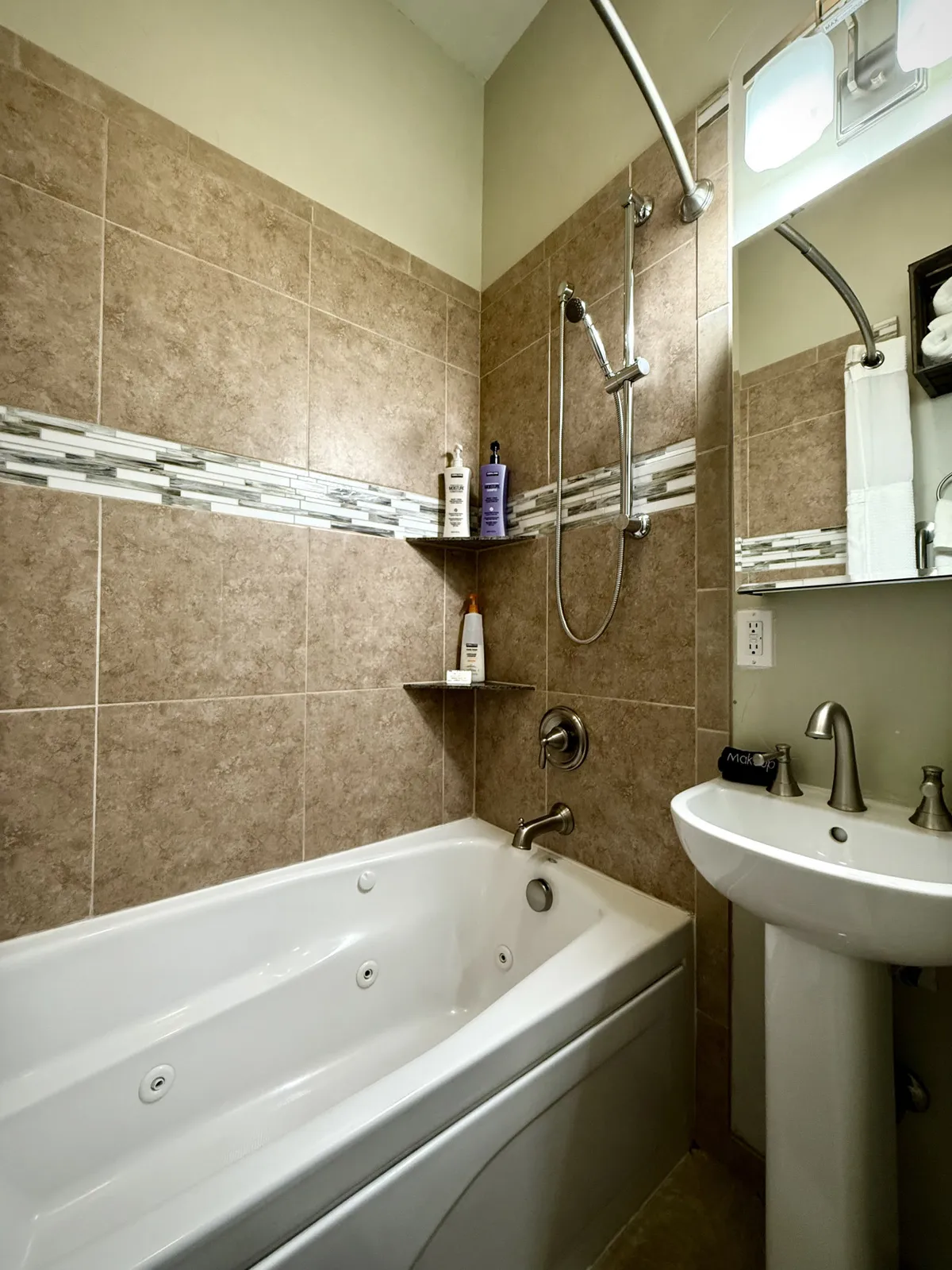 A bright, modern bathroom featuring a whirlpool Jacuzzi tub, a shower fixture, and a sink with a mirror. The clean lines and calming decor evoke a sense of luxury and comfort, making it an ideal place to relax and recharge.