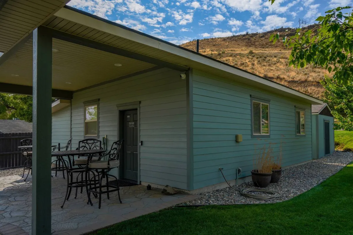 A comfortable patio area with stylish furniture set beside a green exterior wall and a landscaped yard, exuding a relaxed, inviting mood. The patio suggests a perfect spot for al fresco dining, morning coffee, or casual meetings after a productive workday.