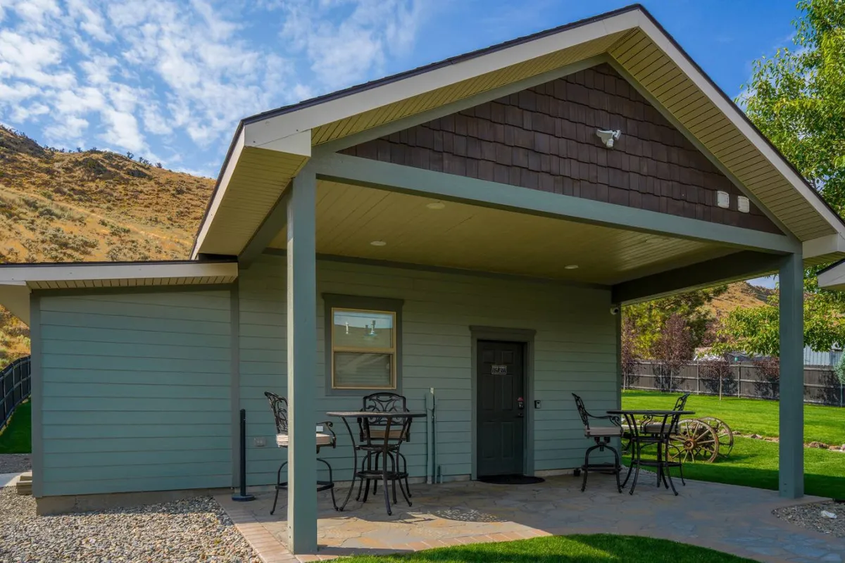 The green cottage exterior with an inviting outdoor seating area set on a green lawn and surrounded by hills, capturing the allure of relaxing outdoors with loved ones as the sun sets or stars emerge.